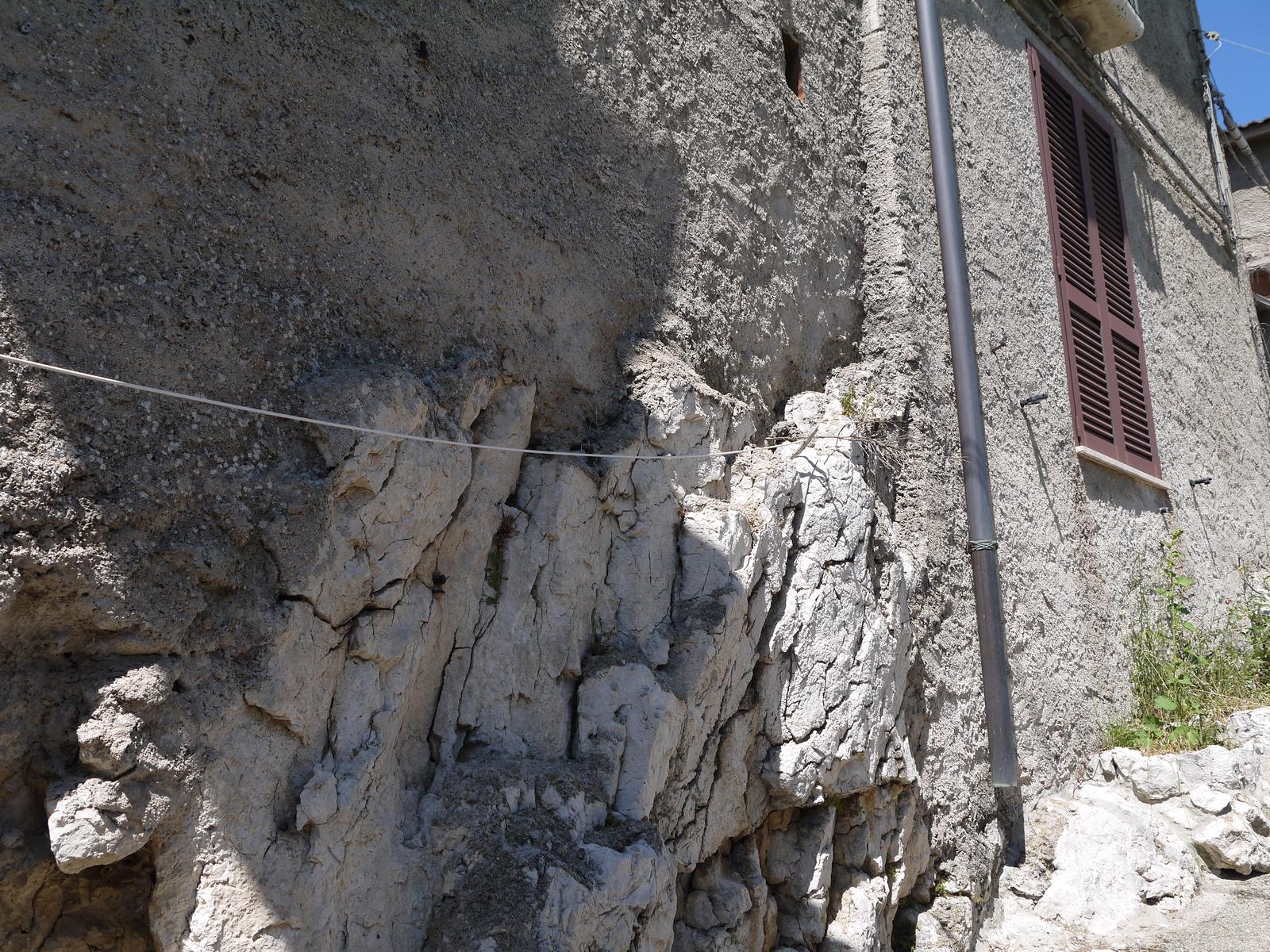 A house wall merging directly into the bare limestone rock it was built against