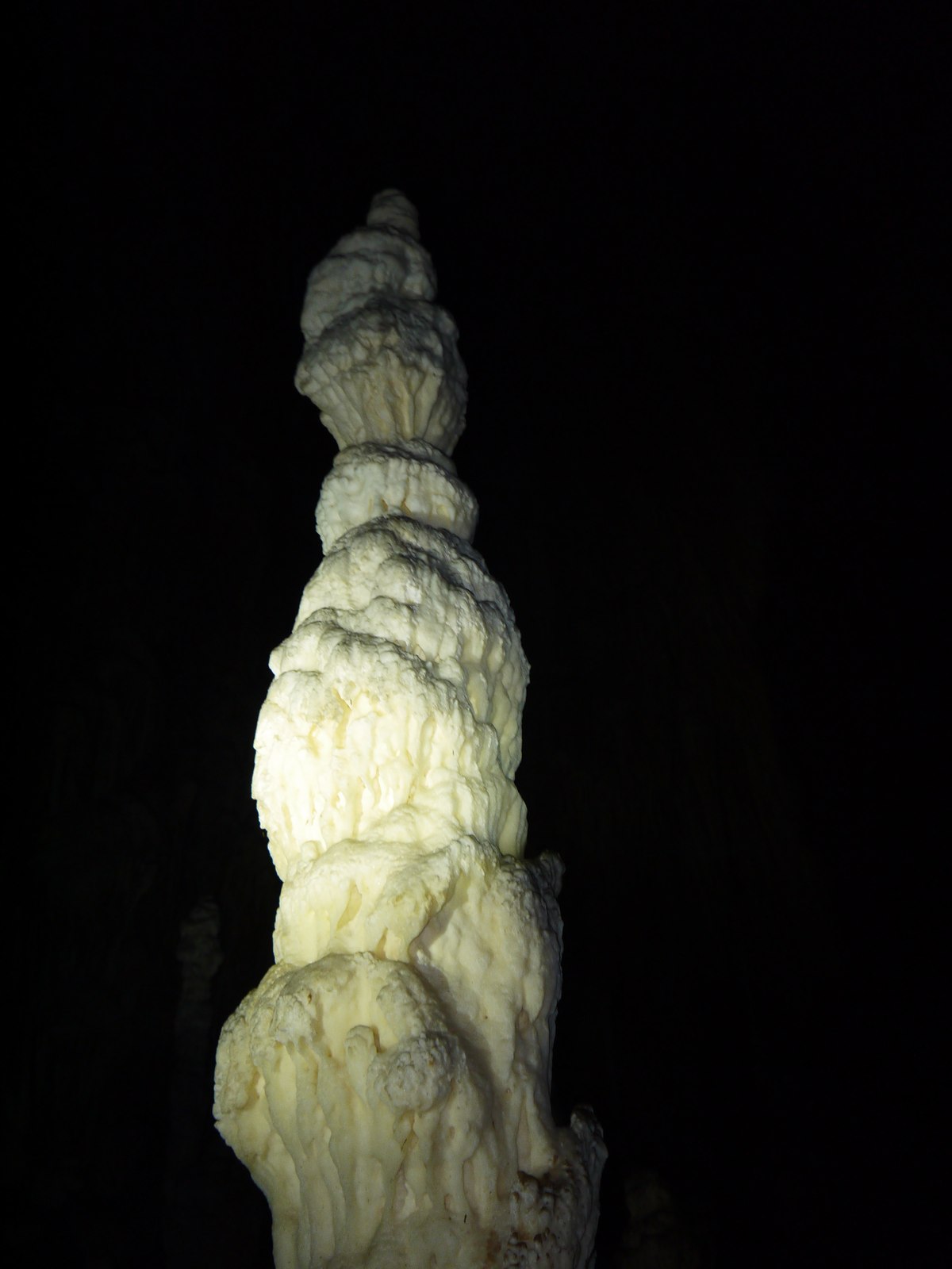 A tall stalagmite lit only by torchlight inside the cave